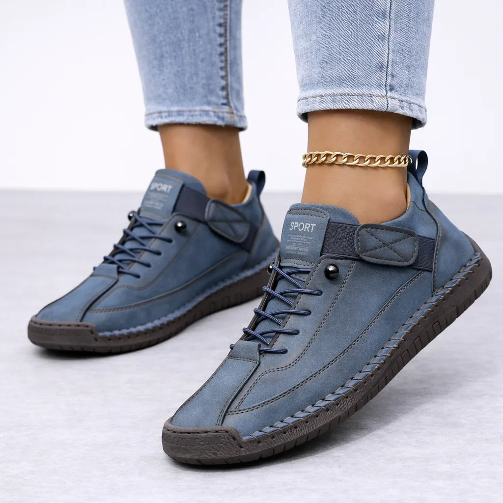 Navy blue suede lace-up trainers with a hook-and-loop ankle strap and brown textured sole, styled with turned-up jeans