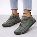 Sage green suede trainers with tan trim detailing and a dark brown stitched outsole, shown from the side on feet