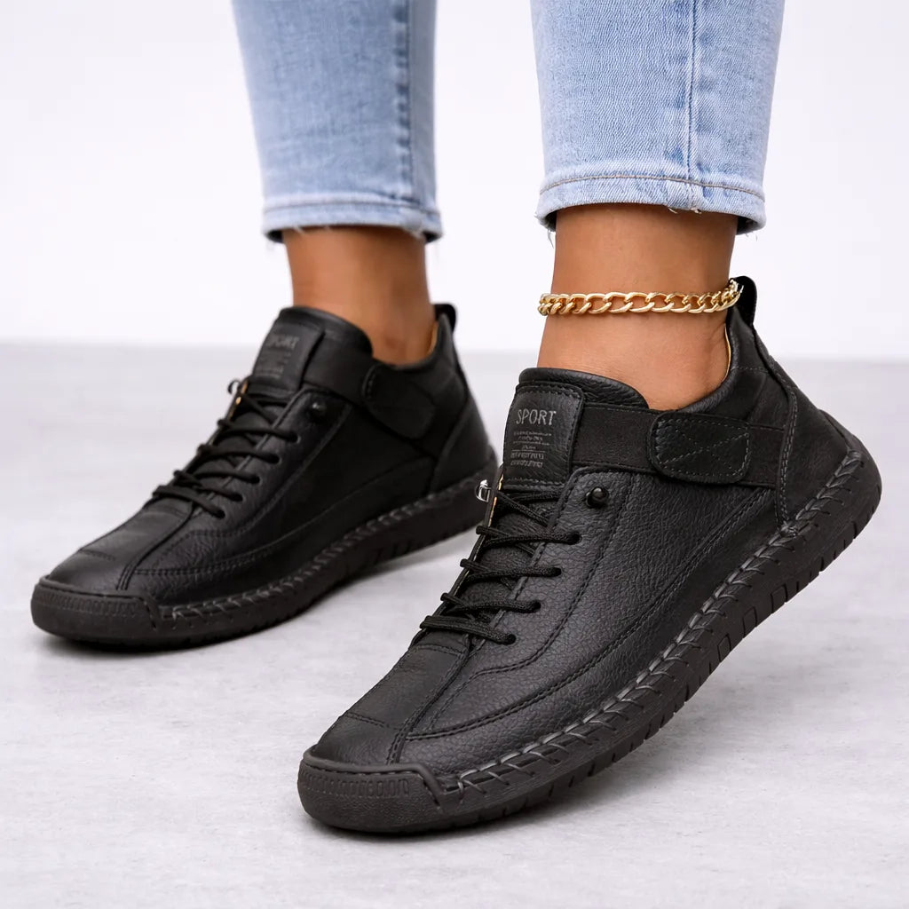 All-black leather lace-up trainers with tonal stitching and a matching ridged sole, worn with cuffed denim jeans