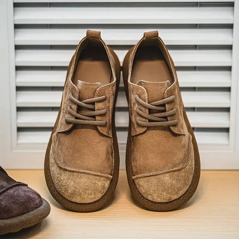 Front view of tan suede derby shoes with contrast lacing, standing side by side against a slatted white panel