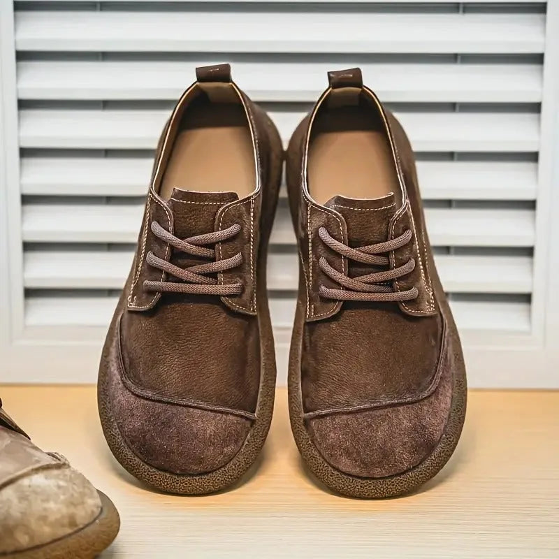 Side view of a tan leather derby shoe with suede overlay held in a hand wearing a wristwatch