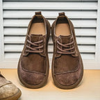 Side view of a tan leather derby shoe with suede overlay held in a hand wearing a wristwatch