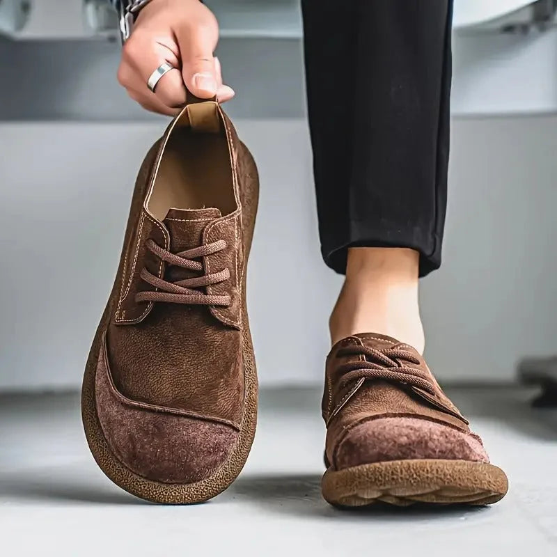 Close-up of a tan suede derby shoe held in hand, showing the beige lacing and stitched seam detail