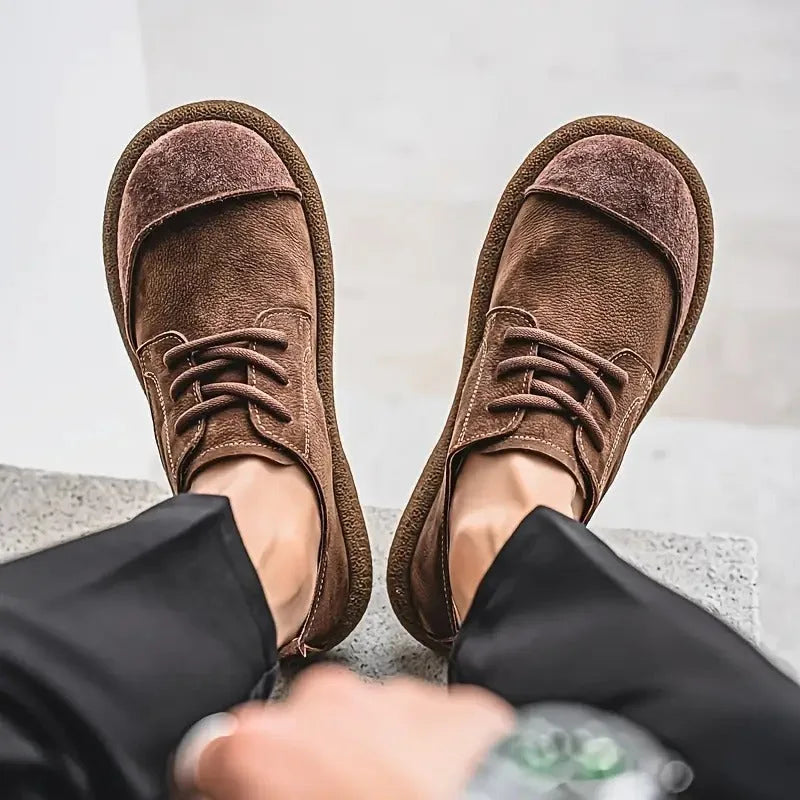 Close-up of a dark brown suede shoe held by its heel loop, showing the tan interior lining and soft footbed