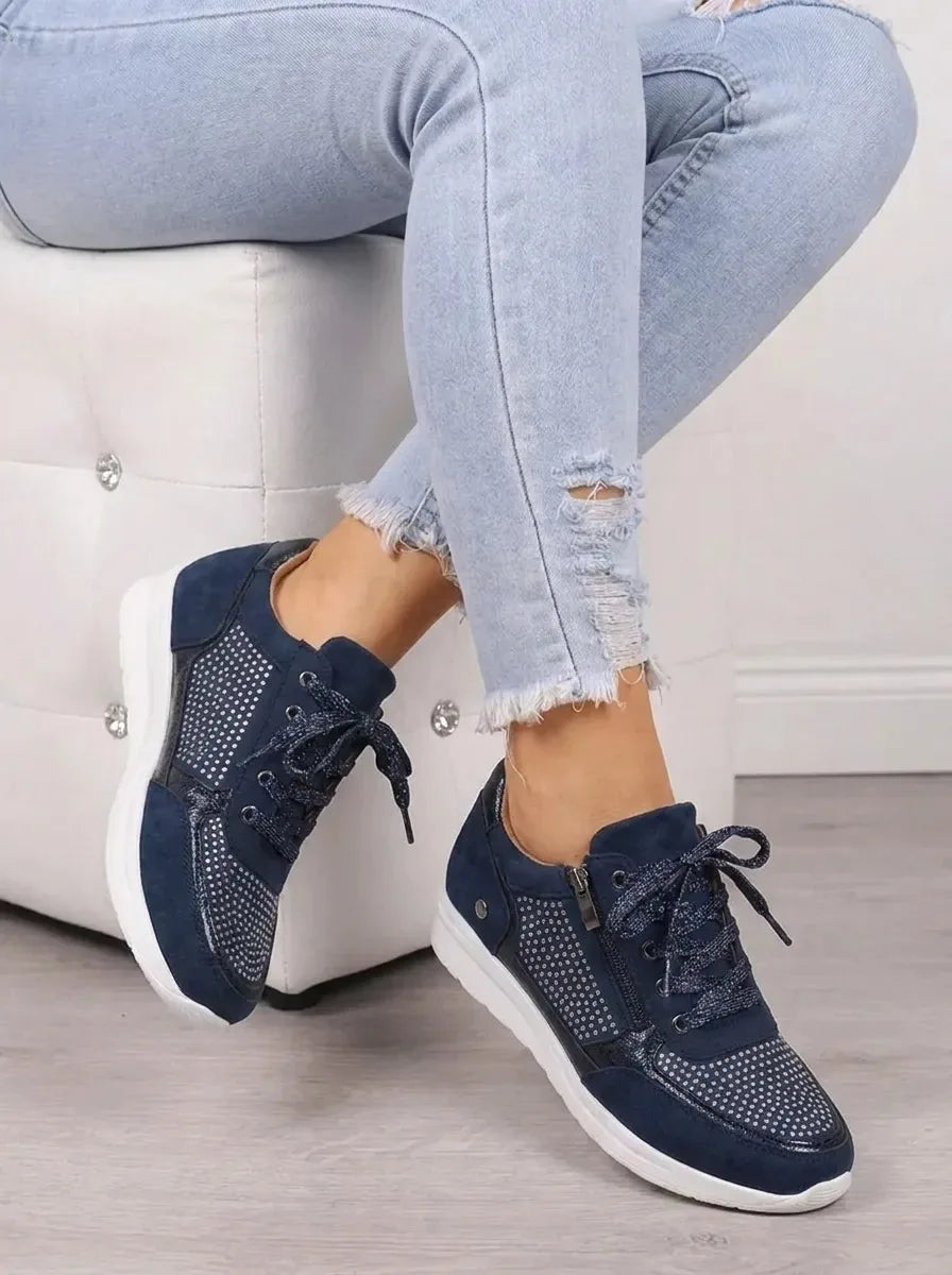 Seated view of navy rhinestone-studded trainers with glitter laces and chunky white outsole