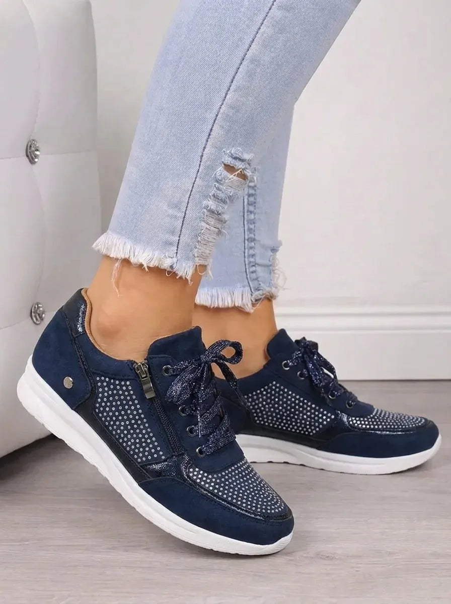 Close-up side angle of navy trainers highlighting the metallic trim, zip pull and diamante detailing