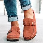 Side view of rust suede slingback clogs with buckle strap and stitched cork-look sole, worn with rolled-up jeans.