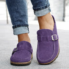 Purple suede mule-style loafers with adjustable side buckle and sturdy sole, shown from the front on model's feet.