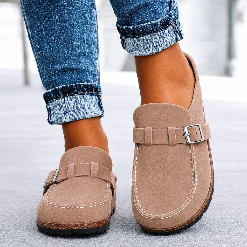 Taupe suede slip-on clogs with buckle trim and stacked sole, close-up front view with cuffed jeans.
