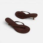Angled view of dark brown suede thong sandals with kitten heel and cushioned footbed on a plain background