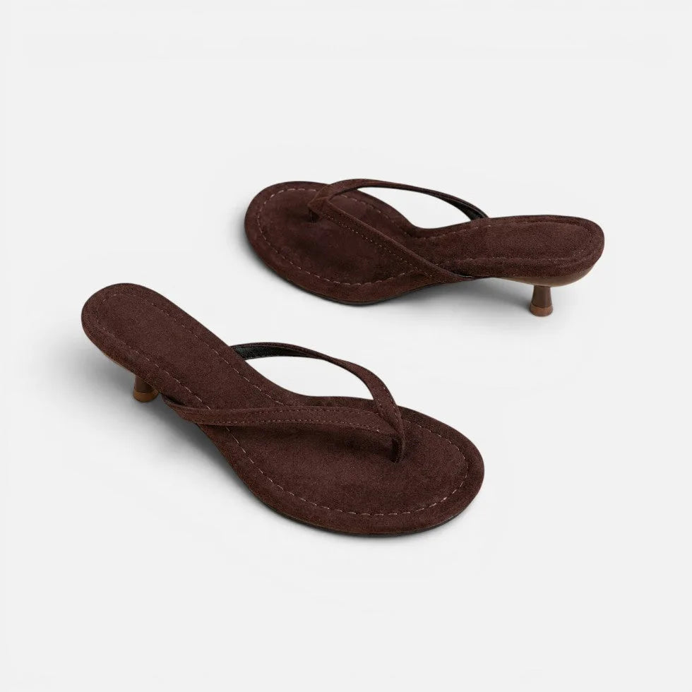 Angled view of dark brown suede thong sandals with kitten heel and cushioned footbed on a plain background