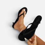 Black suede thong sandals with kitten heel worn on a model's feet, close-up showing toe strap detail