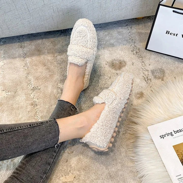 Overhead view of cream teddy fleece loafers worn with grey jeans beside a magazine and gift bag