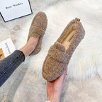 Overhead shot of brown teddy fleece loafers worn on bare feet resting on a cream faux-fur rug