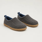 Pair of grey wool-felt slippers with navy fabric pull tabs and blue fleece lining, resting on tan soles