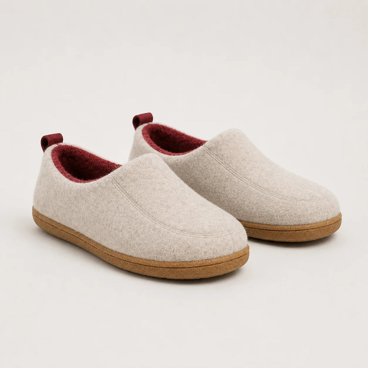 Pair of beige wool-felt slippers with burgundy fleece lining and burgundy pull tabs on tan soles