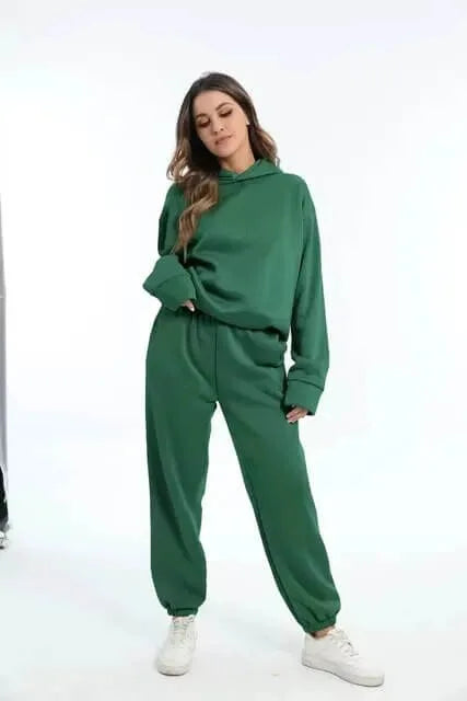 Woman wearing an oversized green hooded tracksuit set with white trainers, side view against a plain backdrop