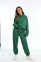 Woman wearing an oversized green hooded tracksuit set with white trainers, side view against a plain backdrop