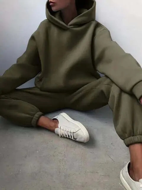 Close crop of a khaki green oversized hoodie and joggers, seated pose showing ribbed cuffs and white trainers