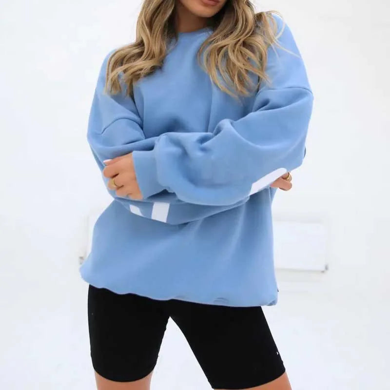 Woman wearing an oversized light blue jumper with white stripe cuff detail and crew neck, arms crossed