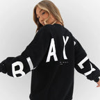 Model in a black oversized jumper with bold white lettering print across the back and sleeves