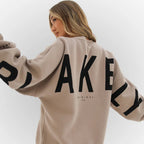 Beige oversized jumper shown from the back with black lettering print and ribbed cuffs
