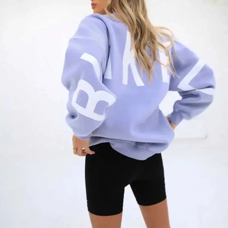 Back view of a light purple oversized jumper with white letter print across the sleeves and ribbed hem