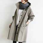 Woman wearing an oversized light grey hooded trench coat with front button placket and a chunky grey scarf