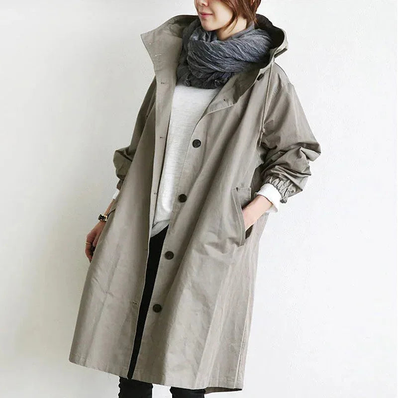 Woman wearing an oversized light grey hooded trench coat with front button placket and a chunky grey scarf