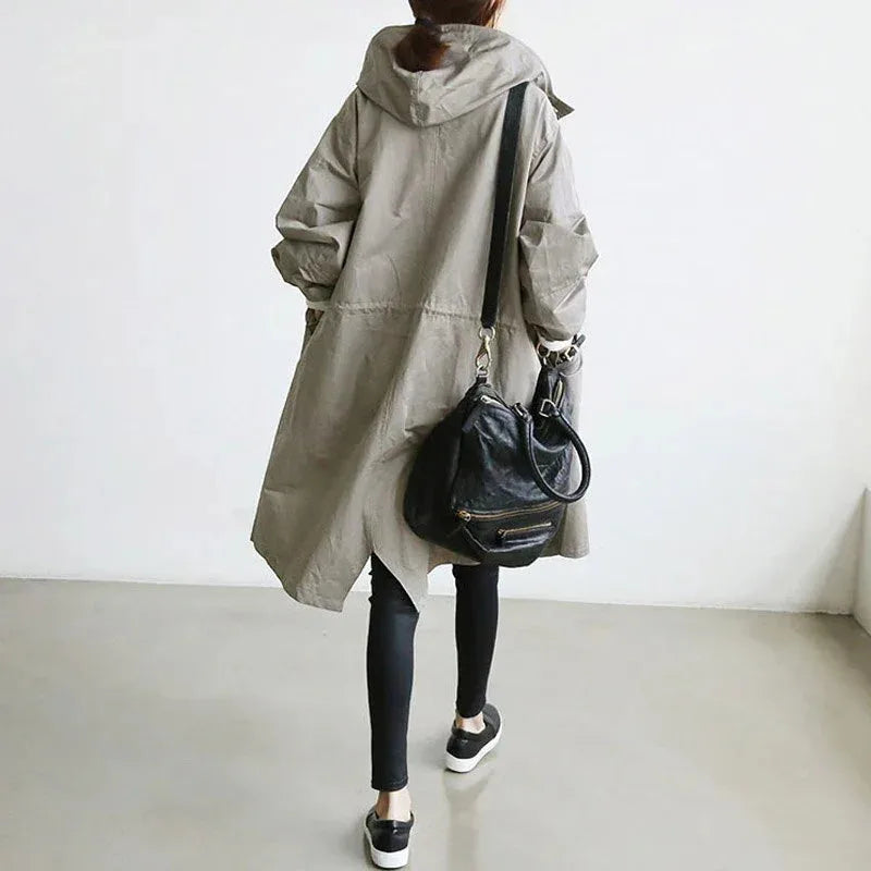 Back view of a grey hooded trench coat with an A-line silhouette worn with a black crossbody bag