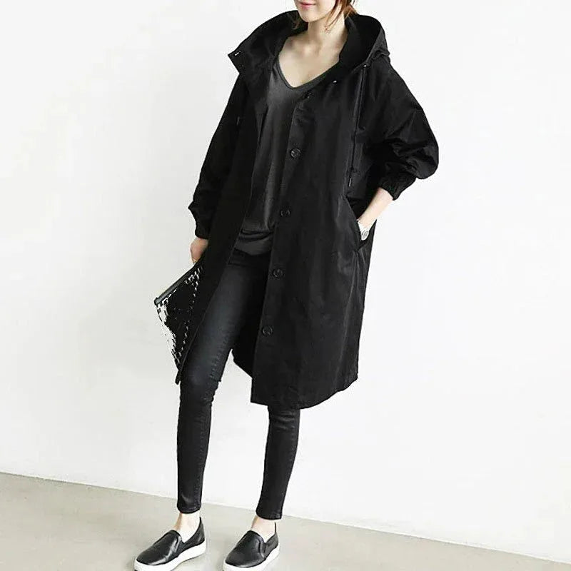 Model in a black oversized hooded longline coat with dropped shoulders and button front, worn open