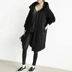 Model in a black oversized hooded longline coat with dropped shoulders and button front, worn open