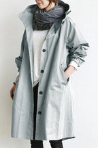 Woman wearing an oversized grey hooded trench coat, unbuttoned over a white jumper and layered scarf