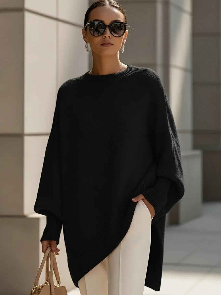 Side angle of the beige knit jumper showing the flowing asymmetrical hem and ribbed sleeve cuffs