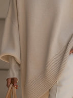 Detail shot of the asymmetric hemline with ribbed trim on the beige oversized poncho jumper