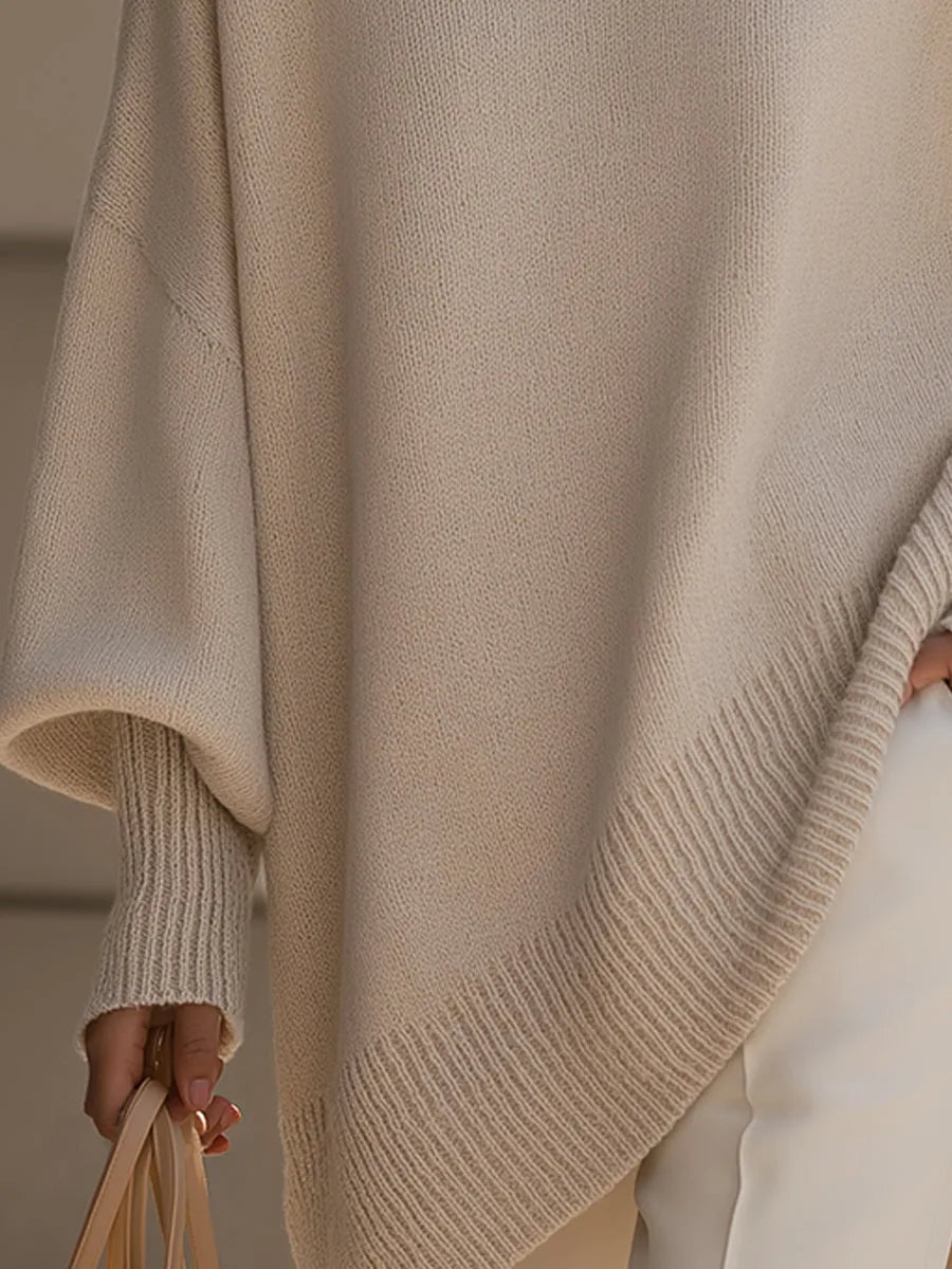 Detail shot of the asymmetric hemline with ribbed trim on the beige oversized poncho jumper