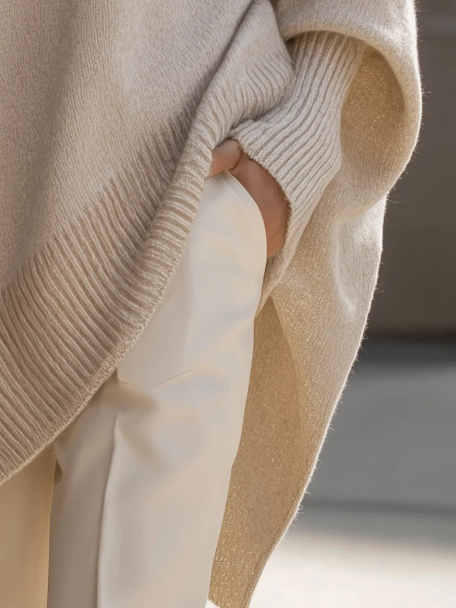 Close-up of a hand tucked into the side split of the beige knit jumper, showing ribbed edge detail