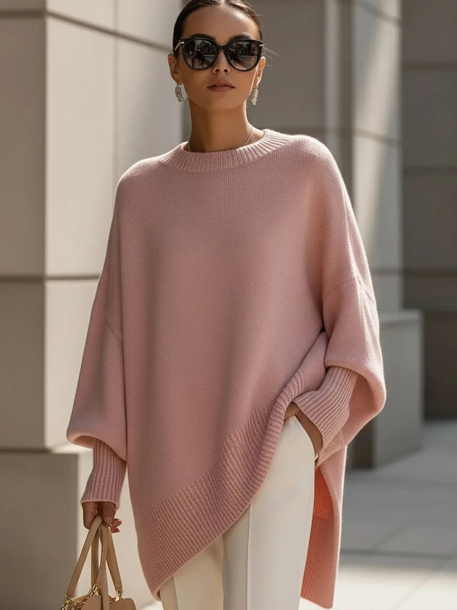 Model wearing the oversized poncho jumper in soft pink with cream trousers and dark sunglasses