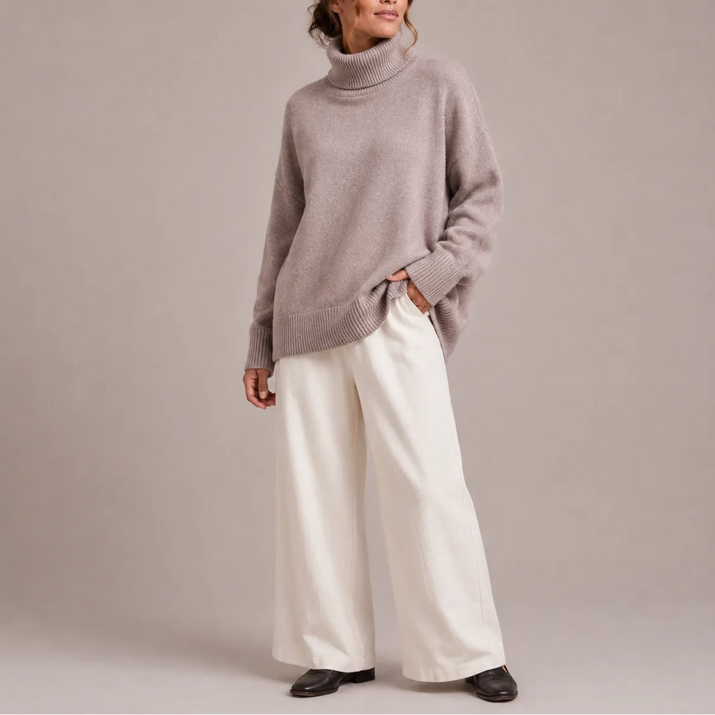 Full-length side view of a light grey oversized polo neck jumper styled with cream trousers and black loafers.