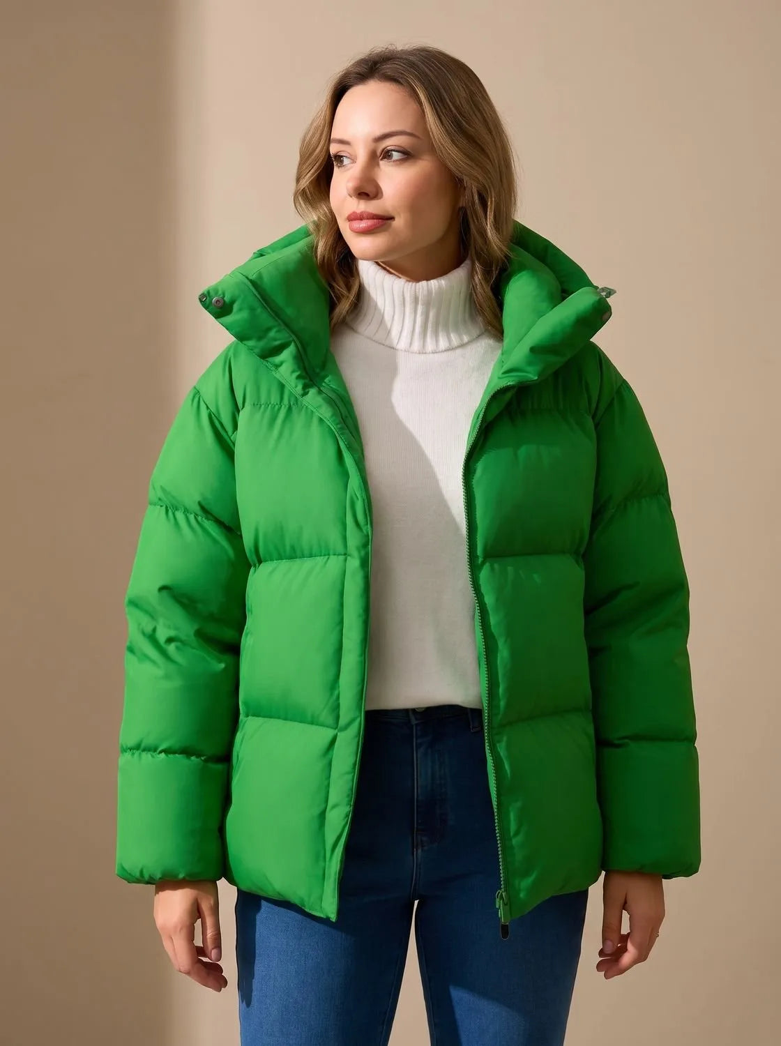 Front view of a model wearing a green oversized quilted puffer jacket with a hood over a cream polo neck jumper.