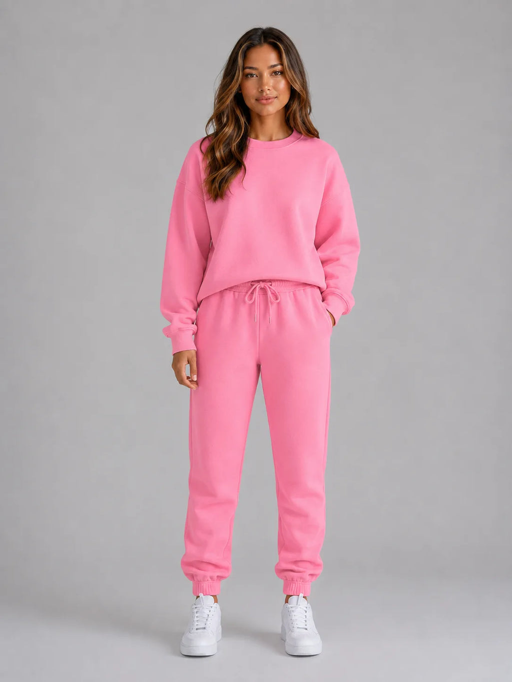 Woman wearing an oversized pink crew neck sweatshirt and matching cuffed joggers with white trainers, front view