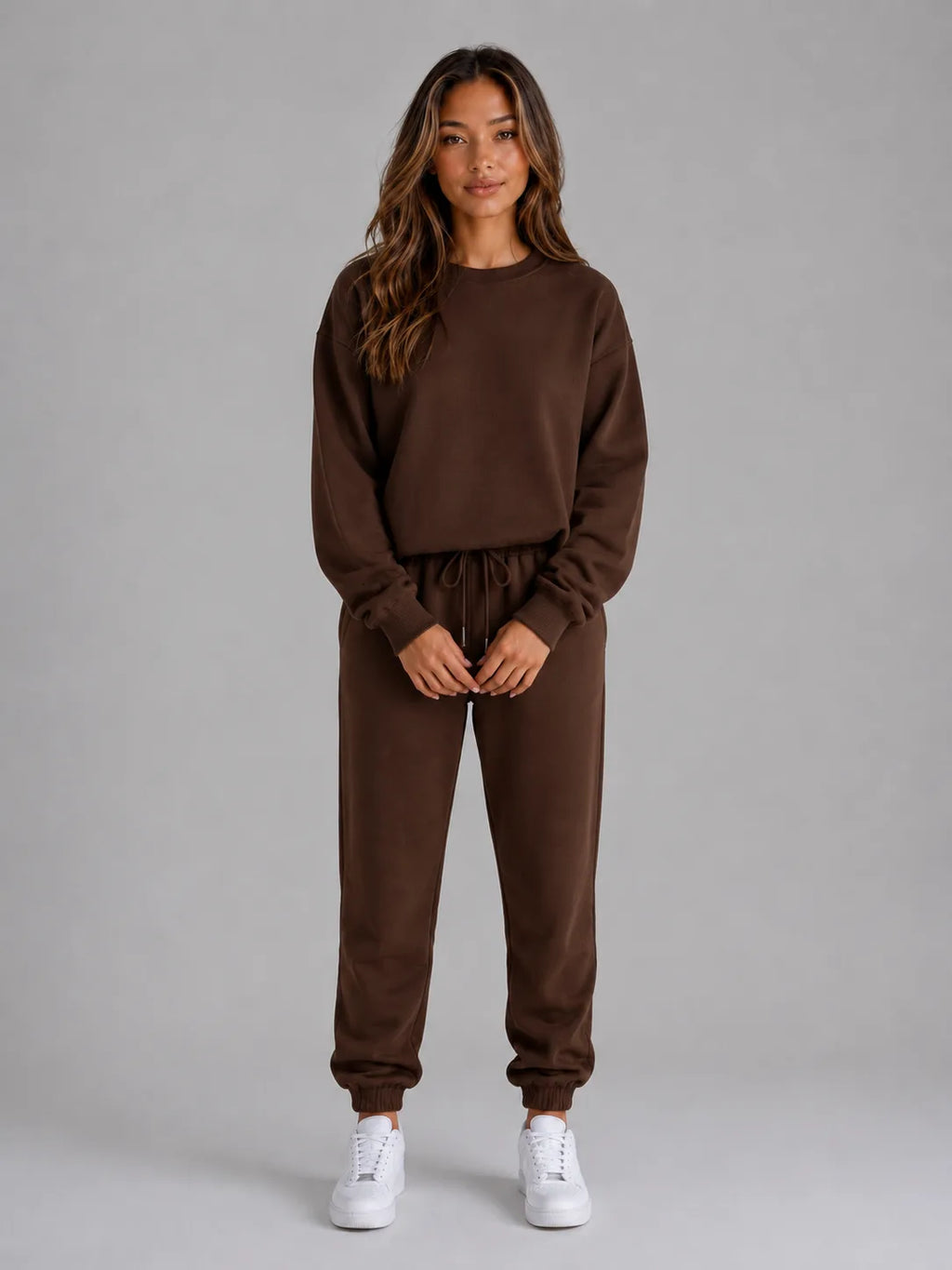 Full-length front view of the oversized tracksuit set in dark brown with white trainers
