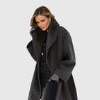 Front view of a charcoal black shawl-collar wool coat, oversized fit with wide lapels, styled with a black polo neck