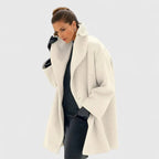 Ivory white oversized wool coat with wide shawl collar, worn open over a black dress, model touching the collar
