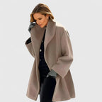 Taupe beige oversized wool coat with wide lapel collar, worn open over black trousers, relaxed drape shown