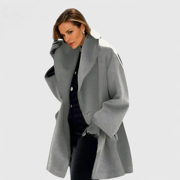 Light grey oversized wool coat with wide shawl collar and dropped shoulders, worn open over a black polo neck