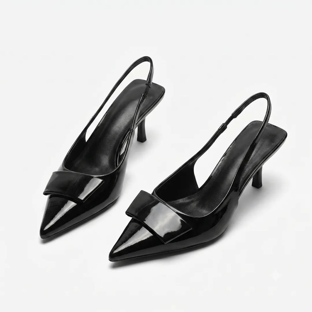 Front angled view of a pair of black patent slingback pumps showing the pointed toe, buckle trim and slim kitten heel