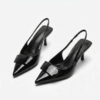 Front angled view of a pair of black patent slingback pumps showing the pointed toe, buckle trim and slim kitten heel