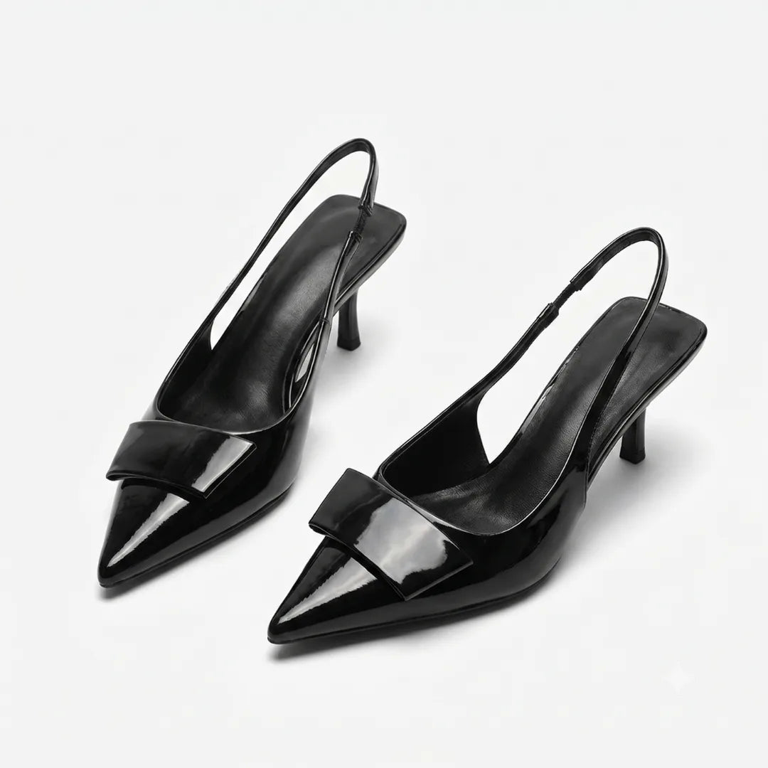 Front angled view of a pair of black patent slingback pumps showing the pointed toe, buckle trim and slim kitten heel
