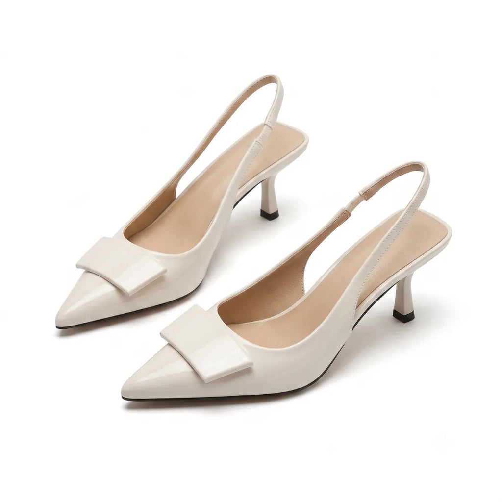 Angled pair shot of cream patent slingback pumps with pointed toe, buckle trim and slender kitten heel on a plain background